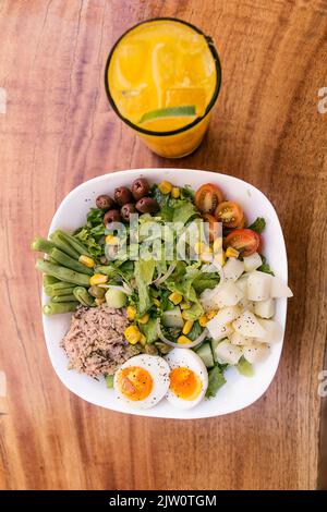 Salade de thon, œuf, pomme de terre, laitue, oignon, tomate, maïs, olives noires et asperges. Servi dans un bol blanc sur une table en bois. Verre à jus d'orange. Healt Banque D'Images