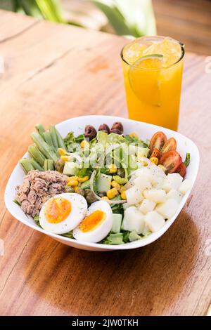 Salade de thon, œuf, pomme de terre, laitue, oignon, tomate, maïs, olives noires et asperges. Servi dans un bol blanc sur une table en bois. Verre à jus d'orange. Healt Banque D'Images