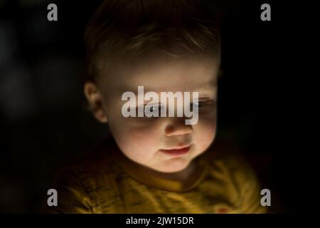 Un jeune garçon aux cheveux blonds et aux yeux bleus regarde vers le bas avec une lumière brillante vers le haut. Banque D'Images