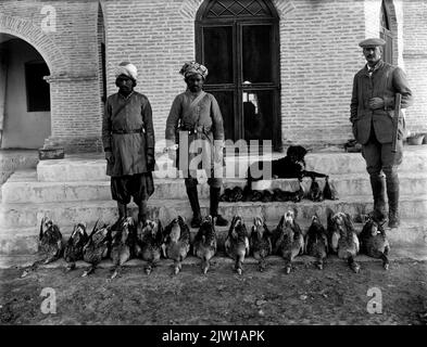 AJAXNETPHOTO. 1919-1920S (ENVIRON). INDE. FRONTIÈRE DU NORD-OUEST. - UN SAC DE JOUR - UN GENTLEMAN EUROPÉEN AVEC FUSIL DE CHASSE (À DROITE) EN TENUE DE CHASSE, UN CHIEN ET DEUX SCOUTS ÉVENTUELLEMENT EN ROBE DE WAZIRISTAN, AVEC LEURS OIES SAUVAGES ET LEURS TROPHÉES DE CANARD DISPOSÉS SUR LES MARCHES DU BÂTIMENT À L'ARRIÈRE. PHOTOGRAPHE:INCONNU © IMAGE NUMÉRIQUE COPYRIGHT AJAX VINTAGE PICTURE LIBRARY SOURCE: AJAX VINTAGE PICTURE LIBRARY COLLECTION REF:1920 4 2 Banque D'Images