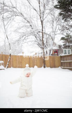 Un bébé caucasien de 12 mois en costume de neige jette de la neige dans l'air. Banque D'Images