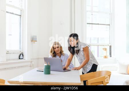 Des collègues multiraciaux planifiant une stratégie d'entreprise par rapport à un ordinateur portable dans un bureau créatif Banque D'Images