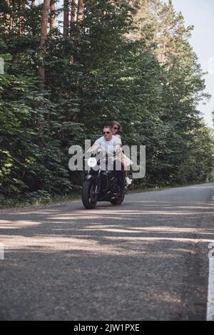 Un jeune couple heureux fait une moto sur une route asphaltée dans la forêt, la liberté et la vitesse Banque D'Images