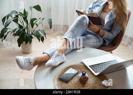 Méconnaissable Jeune femme prenant des notes dans un ordinateur portable assis au travail à la maison, au travail à distance Banque D'Images