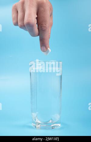 main met une pilule dans un verre sur un fond bleu, traitement de mal de tête. Banque D'Images