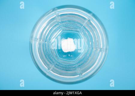 la pilule se dissout dans un verre d'eau sur un fond bleu vue du dessus. Banque D'Images
