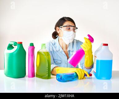 Gâchée pour le choix sur ce qu'il faut utiliser pour les corvées. Une jeune femme qui tient plusieurs bouteilles de détergents. Banque D'Images