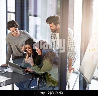 Ils produisent le meilleur travail ensemble. Un groupe de collègues travaillant ensemble sur un ordinateur portable dans un bureau. Banque D'Images