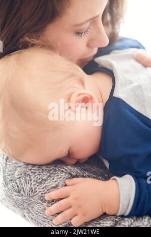 Tenant serré à sa plus grande joie. Une mère tenant son bébé garçon endormi à la maison. Banque D'Images
