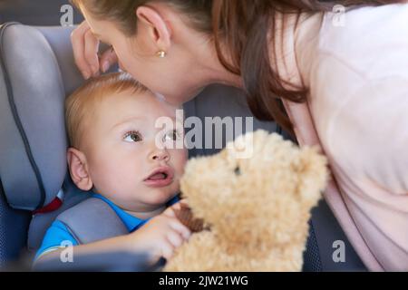 J'espère qu'il s'est arrêté à la boutique de jouets, maman. Une mère embrassant son bébé garçon assis dans un siège de voiture. Banque D'Images