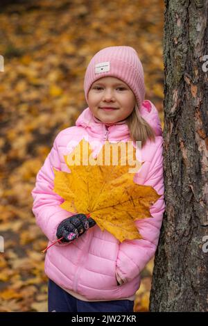 Une fille tient une grande feuille d'érable jaune dans ses mains. Banque D'Images