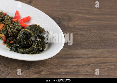 Jusqu'à Daun Singkong, feuilles de manioc Stir Fry farcies à la noix de coco râpée, au pétai Cina et à l'anchois salé, menu quotidien indonésien traditionnel. Station santé Copy Banque D'Images