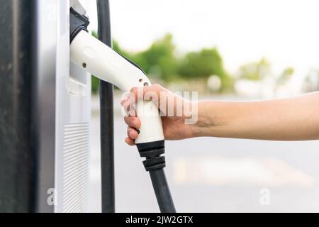 Crop anonyme femme mettant la buse de pompe à carburant dans le distributeur après le ravitaillement en voiture à la station-service en ville Banque D'Images