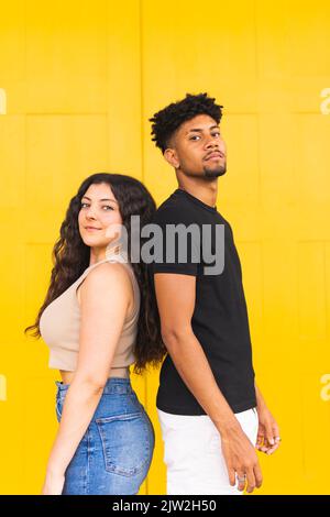 Portrait d'un jeune couple confiant debout dos à dos contre la porte jaune Banque D'Images