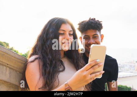 Jeune couple souriant regardant un smartphone tout en se tenant sur des marches en ville Banque D'Images