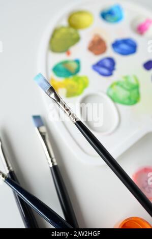 Depuis le dessus des palettes en plastique blanc avec des taches sèches de peinture colorée placées près des brosses sur la table en atelier Banque D'Images