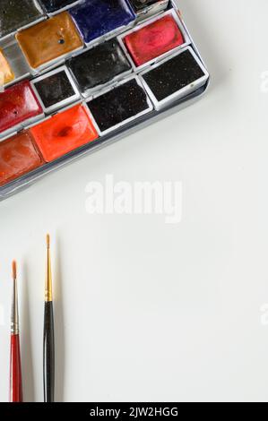 Depuis le dessus des palettes en plastique blanc avec des taches sèches de peinture colorée placées près des brosses sur la table en atelier Banque D'Images