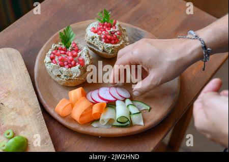 De dessus de la personne anonyme mettant des légumes frais coupés sur plaque de bois avec des sandwiches végétariens faits de pain et de pate de champignons garni Banque D'Images