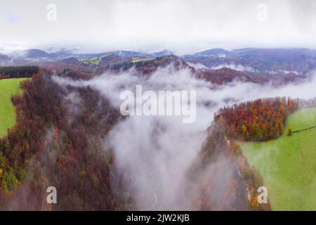 Vue aérienne à couper le souffle sur les nuages flottant sur les montagnes avec des forêts d'automne luxuriantes par temps brumeux Banque D'Images