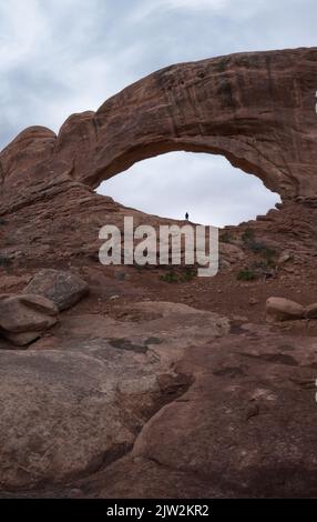 Touriste admirant la vue à couper le souffle à angle bas de la formation de pierre naturelle appelée Window Arch situé contre le ciel couvert le jour terne à Arches National Banque D'Images