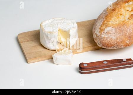 Délicieux fromage camembert placé sur une planche à découper en bois près du pain et du couteau sur fond blanc Banque D'Images