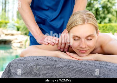 Bonne cliente blonde souriante pendant que le petit masseur se fait masser pendant la séance de spa sur le complexe Banque D'Images