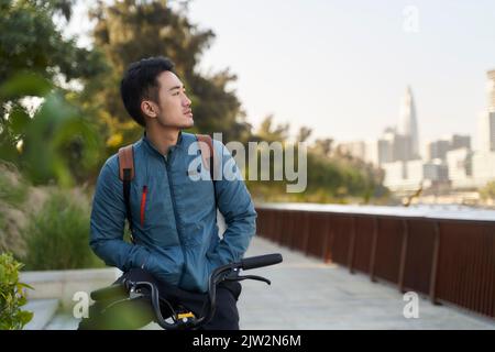 jeune homme asiatique assis à vélo et regardant la vue dans le parc de la ville Banque D'Images