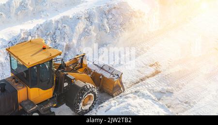 Un gros tracteur orange élimine la neige de la route et dégage le trottoir. Nettoyage et déneigement des routes de la ville en hiver. Déneigement a Banque D'Images