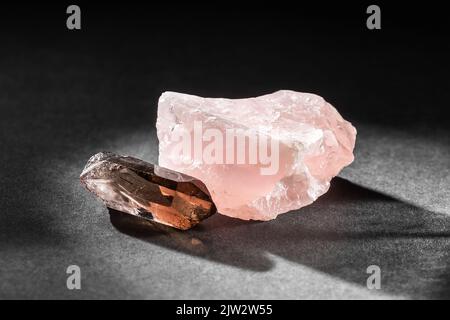 Échantillons de quartz rose rugueux non coupés et de quartz fumé ou de quartz Rauchquartz, rétroéclairés de l'arrière-plan sur fond sombre. Collection géologique de pierres minérales Banque D'Images