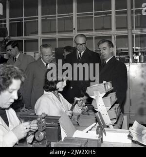 1960s, historique, visite de cadres de l'entreprise dans une usine d'ingénierie légère, en regardant les employées en manteaux blancs en train de travailler, Fife, Écosse, Royaume-Uni. La montée de Silicon Glen a commencé en 1943 lorsque Ferranti, une entreprise d'ingénierie et d'équipement électriques, s'est déplacée de Manchester au nord de la frontière. Peu à peu en 50s et 60s, des entreprises étrangères y ont créé une usine de production, dont IBM et le secteur électronique écossais by1990, connu sous le nom de Silicon Glen, en était à son apogée. Banque D'Images