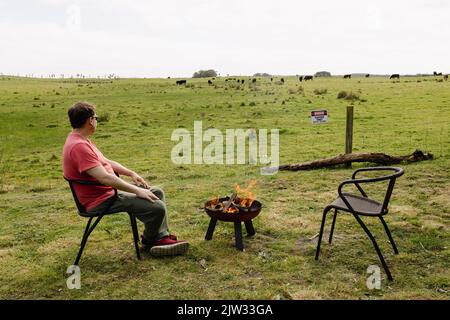 Un homme assis près d'un feu éclairé à côté d'un enclos en Australie Banque D'Images