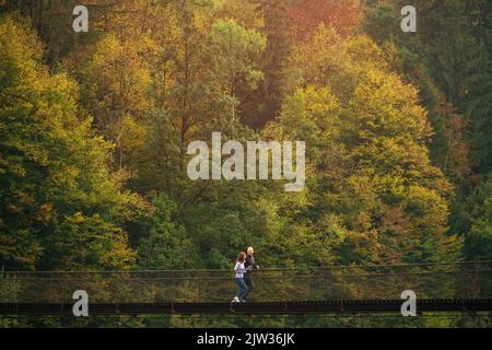 Entraînement tôt le matin. Une jeune famille sportive effectue un jogging matinal sur un pont suspendu, sur fond de forêt montagneuse. Concept d'actif Banque D'Images