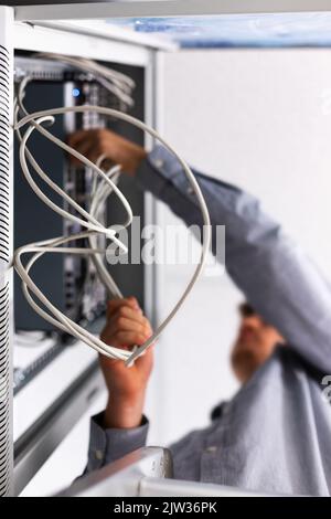 Un homme méconnaissable installe et connecte le câble Internet à la boîte à fusibles. Vue du dessous gros plan des fils torsadés blancs dans les mains d'un homme qui pose le câblage Banque D'Images