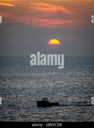 Bateau de pêche qui rentre à la maison après une dure journée de pêche avec le soleil se coucher à l'horizon. Banque D'Images