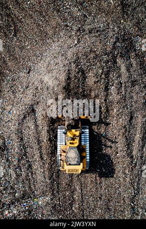 Une vue aérienne d'un bulldozer industriel qui déplace les déchets ménagers et le chou sur un grand site d'enfouissement Banque D'Images