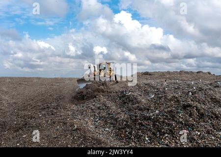 Une machine à bulldozer qui déplace les déchets et les ordures ménagères sur un grand tas de décharges sanitaires Banque D'Images