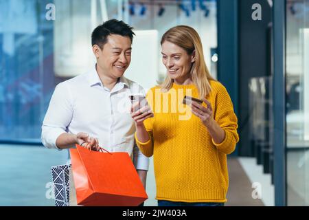 Divers couple d'acheteurs asiatique homme et femme magasiner pour des vêtements à l'intérieur du magasin souriant et heureux tenant la carte de crédit de banque et les achats colorés Banque D'Images
