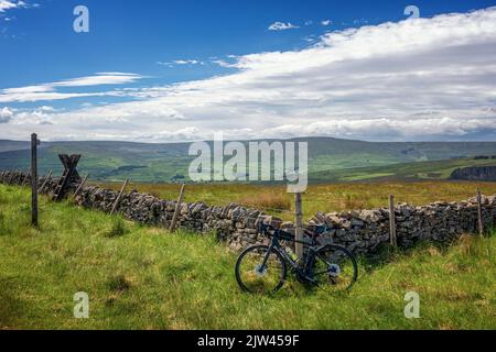 Vue sur la Weardale Valley et de l'autre côté de Cross est tombé du sommet de Peat Hill en vélo escalade avec un vélo de route incliné contre une vieille pierre Banque D'Images