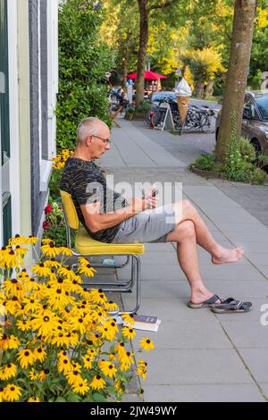 Homme se relaxant entre un petit jardin en façade en face de la vieille maison de ville à Kerklaan dans la ville de Groningen aux pays-Bas. Banque D'Images