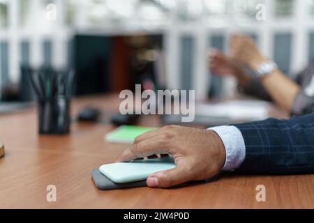 Gros plan d'un homme d'affaires tenant un smartphone sur une table pendant la réunion Banque D'Images