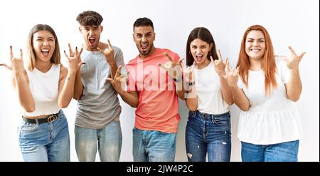 Groupe de jeunes amis se tenant ensemble sur un fond isolé criant avec une expression folle faisant le symbole du rock avec les mains vers le haut. Music star. Heavy mu Banque D'Images