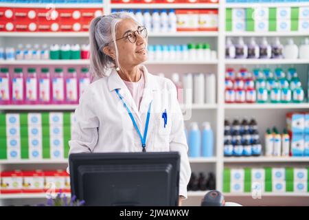 Femme d'âge moyen avec tatouages travaillant à la pharmacie drugstore regardant loin à côté avec le sourire sur le visage, l'expression naturelle. Riant confiant. Banque D'Images