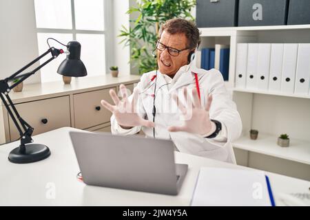Médecin senior homme travaillant sur rendez-vous en ligne peur et terrifié avec l'expression de peur arrêter le geste avec les mains, criant dans le choc. Concept de panique. Banque D'Images