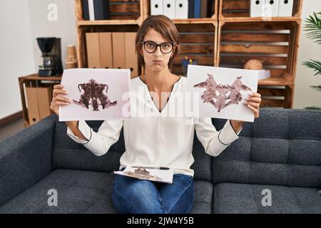 Brunette femme travaillant avec le test rorschach à la clinique de psychologie puffant les joues avec le visage drôle. Bouche gonflée avec de l'air, attrapant l'air. Banque D'Images