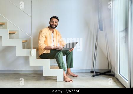 Utilisateur indien heureux assis à la maison à l'aide d'un ordinateur portable travaillant à distance. Banque D'Images