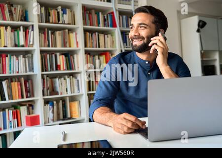 Homme d'affaires indien souriant assis au bureau parlant au téléphone pour passer un appel. Banque D'Images