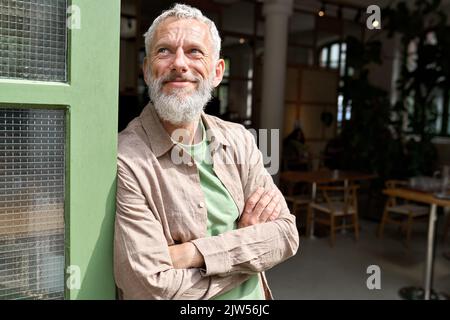 Heureux confiant européen vieux propriétaire de petite entreprise debout à l'extérieur du café. Banque D'Images