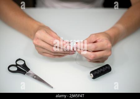 Femme filant l'aiguille à coudre à la table, gros plan. Banque D'Images