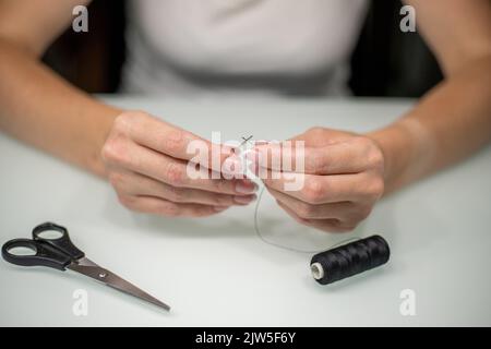 Femme filant l'aiguille à coudre à la table, gros plan. Banque D'Images