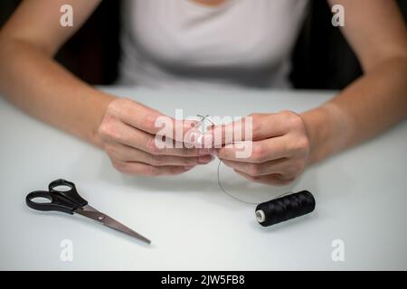 Femme filant l'aiguille à coudre à la table, gros plan. Banque D'Images